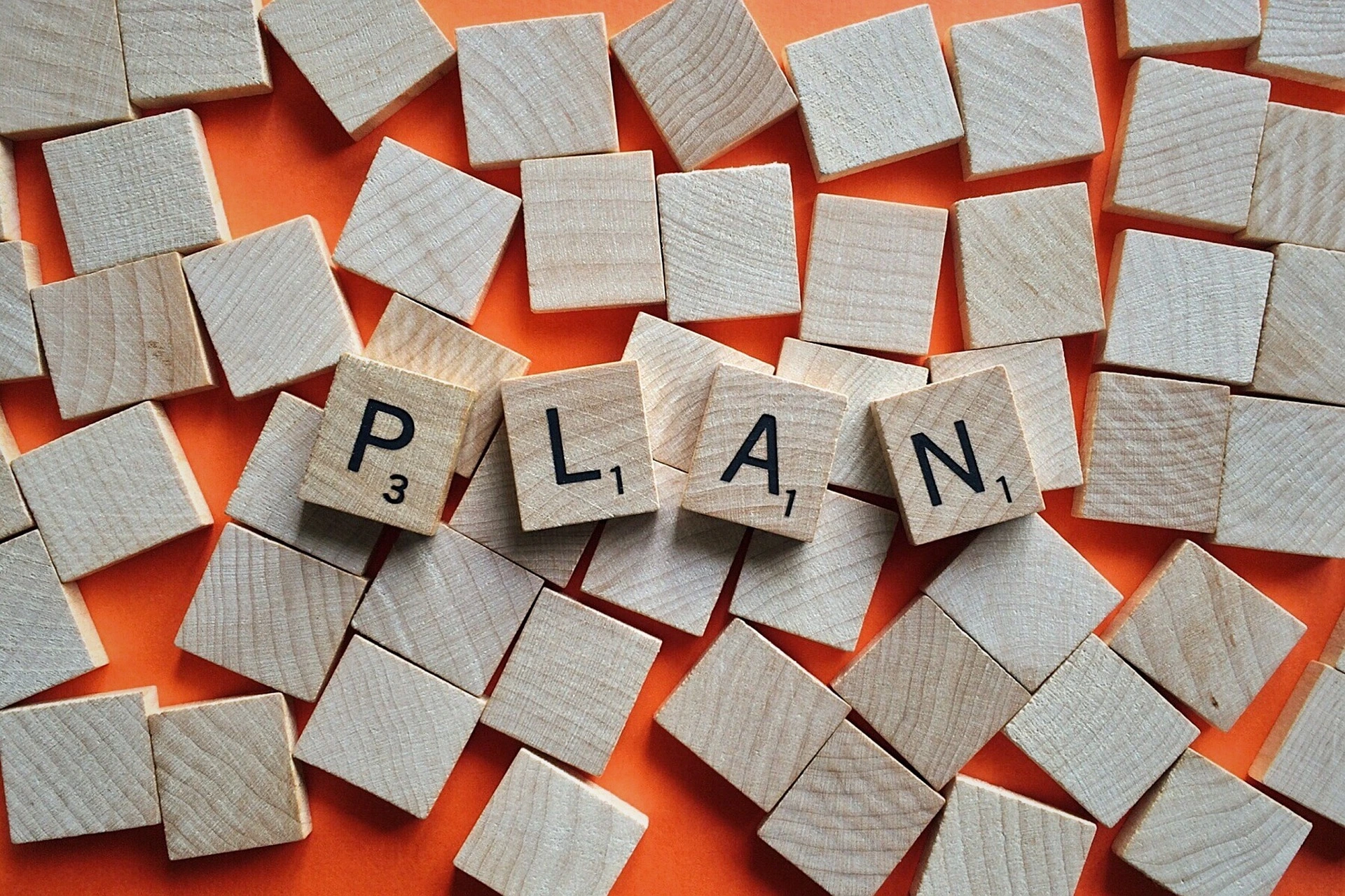 Scrabbles pieces scattered around a table, with 4 tiles on top clearly resembling the word Plan.