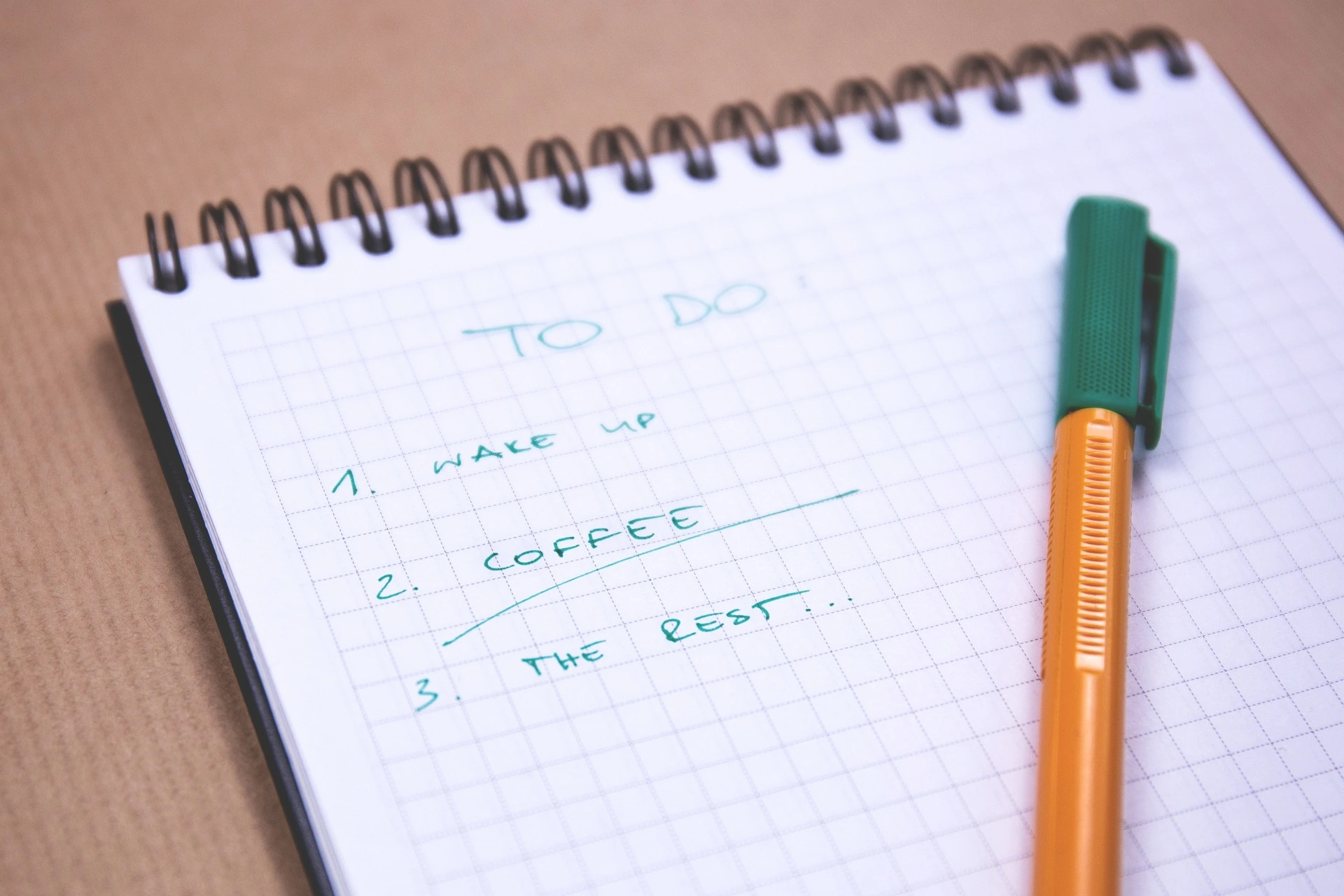 Notepad with a pen on top, containing a to-do list that says 1. Wake Up. 2. Coffee. 3. The rest.